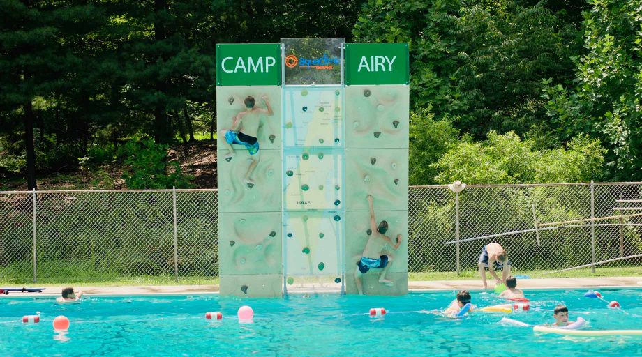 Airy campers climbing rock wall by pool